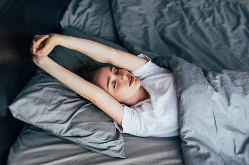 Woman stretching in bed after waking up, in grey bedding