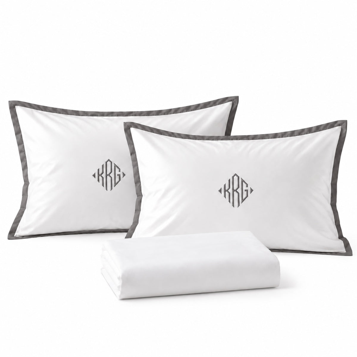 Close-up of TYPEFACE 1 pillowcases with grey satin border and diamond monogram embroidery, with folded white sheet