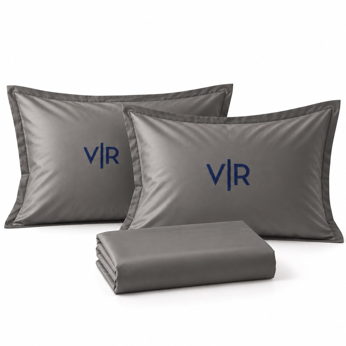 Close-up of TYPEFACE 13 space grey sateen pillowcases with navy monogram embroidery and folded sheet