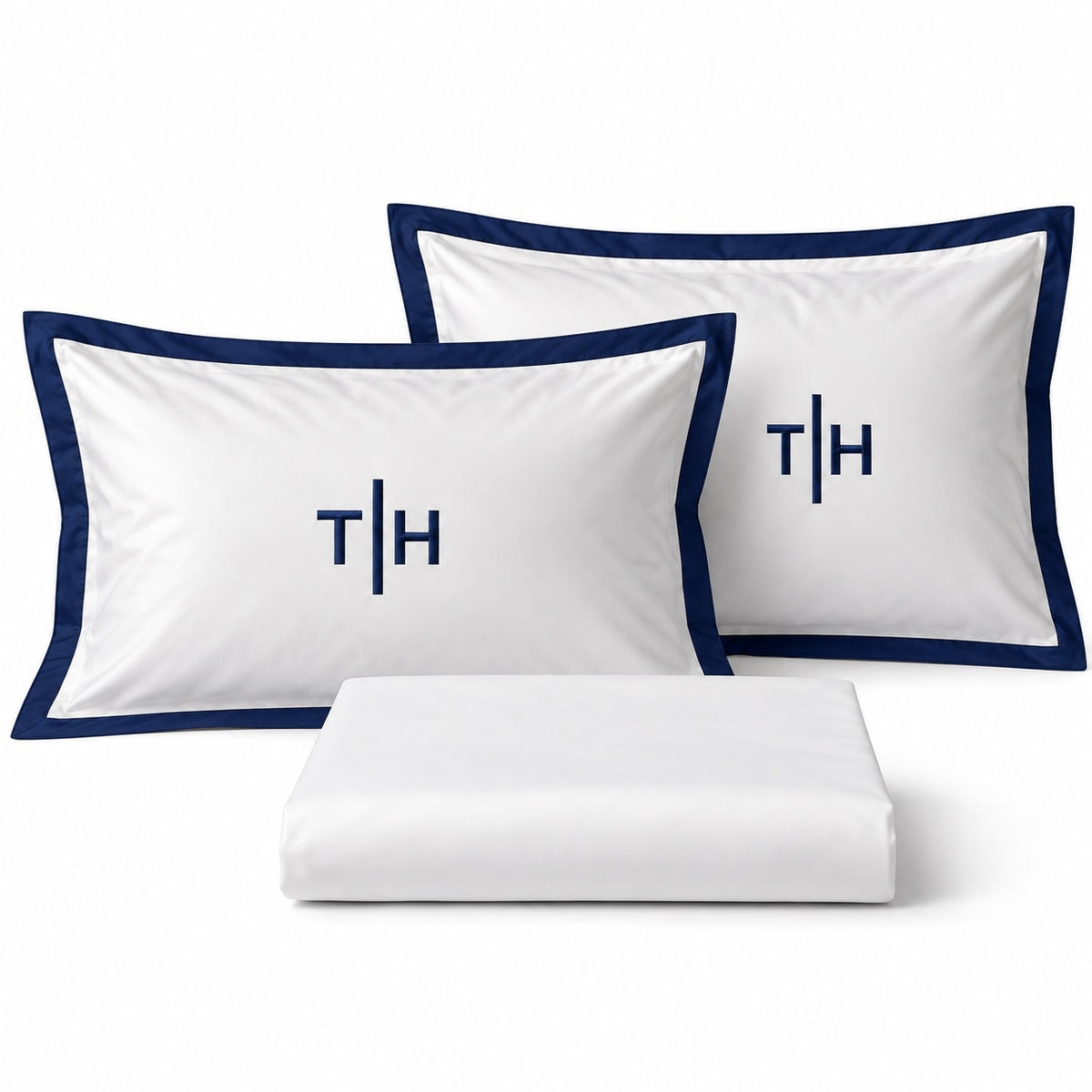 Close-up of TYPEFACE 3 white pillowcases with navy blue border and navy monogram embroidery, with folded sheet
