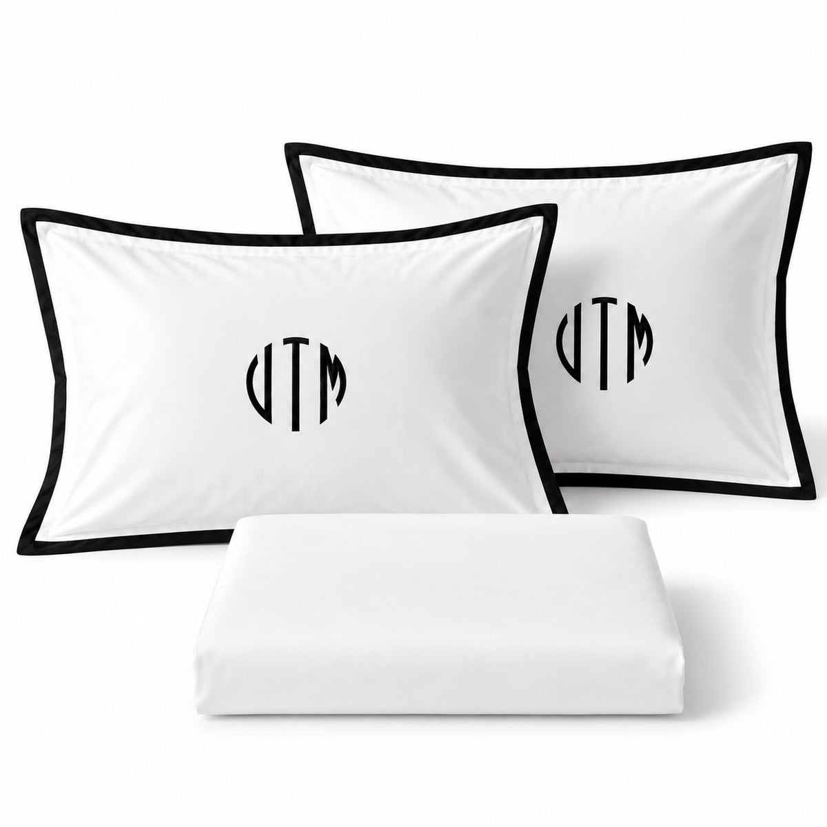 Close-up of TYPEFACE 6 white pillowcases with black border and black circle monogram embroidery, with folded sheet