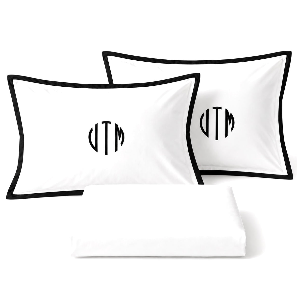 Close-up of TYPEFACE 7 white sateen pillowcases with black border and black circle monogram, with folded sheet