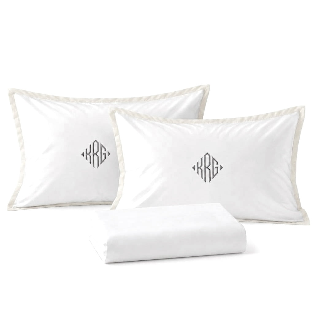 Close-up of TYPEFACE 8 white sateen pillowcases with ivory border and grey diamond monogram, with folded sheet