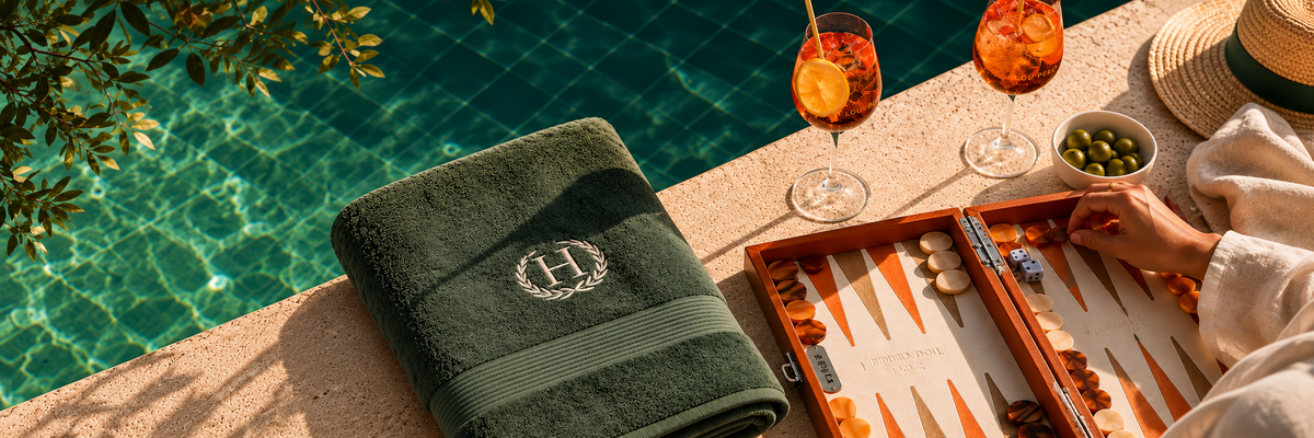 Monogrammed green organic cotton bath towel by BEDLAM beside a pool with a backgammon set and spritz
