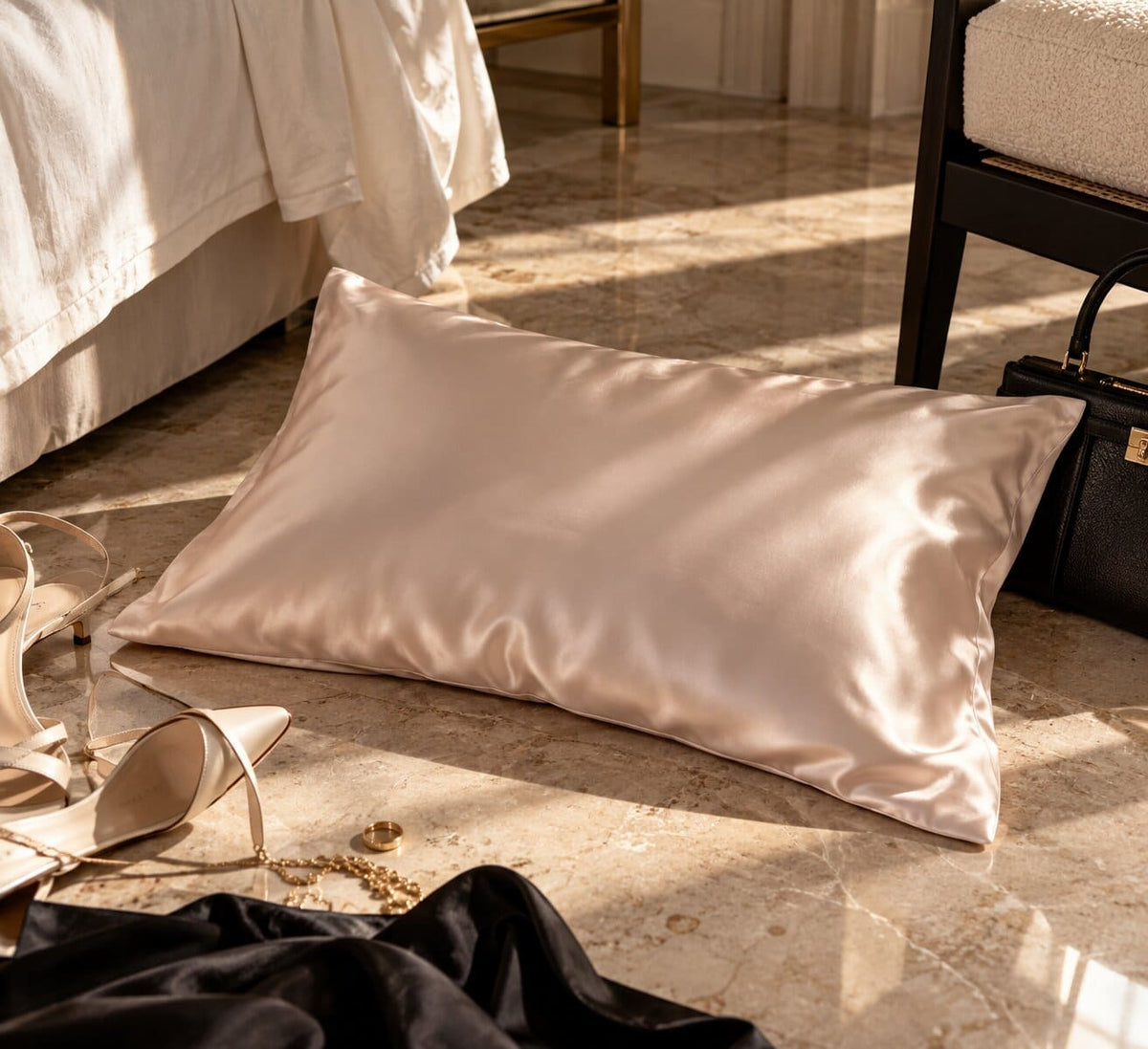 Rose gold mulberry silk pillowcase on a marble floor beside heels and gold jewellery