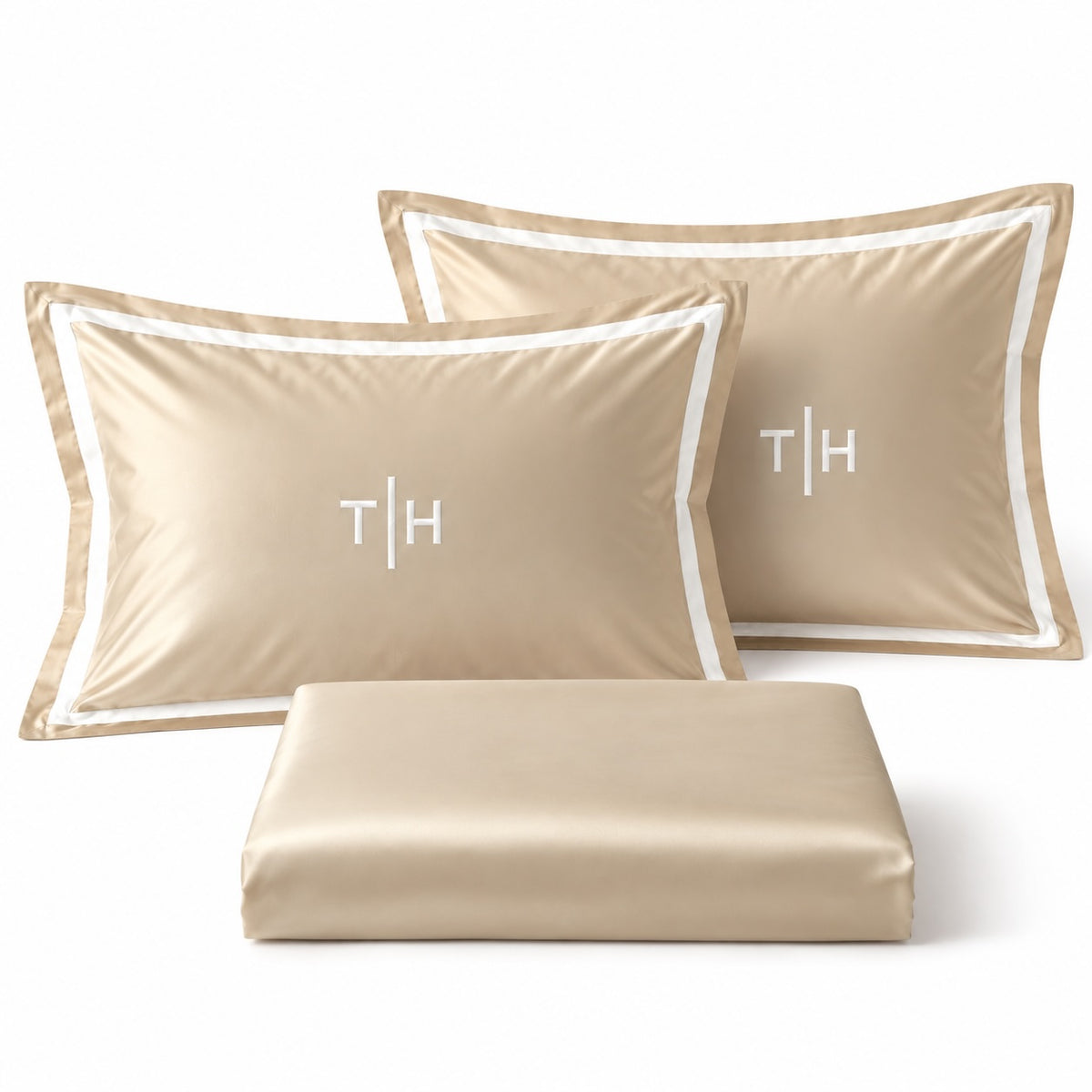 Close-up of TYPEFACE 2 beige sateen pillowcases with white satin border and embroidered monogram, with folded sheet