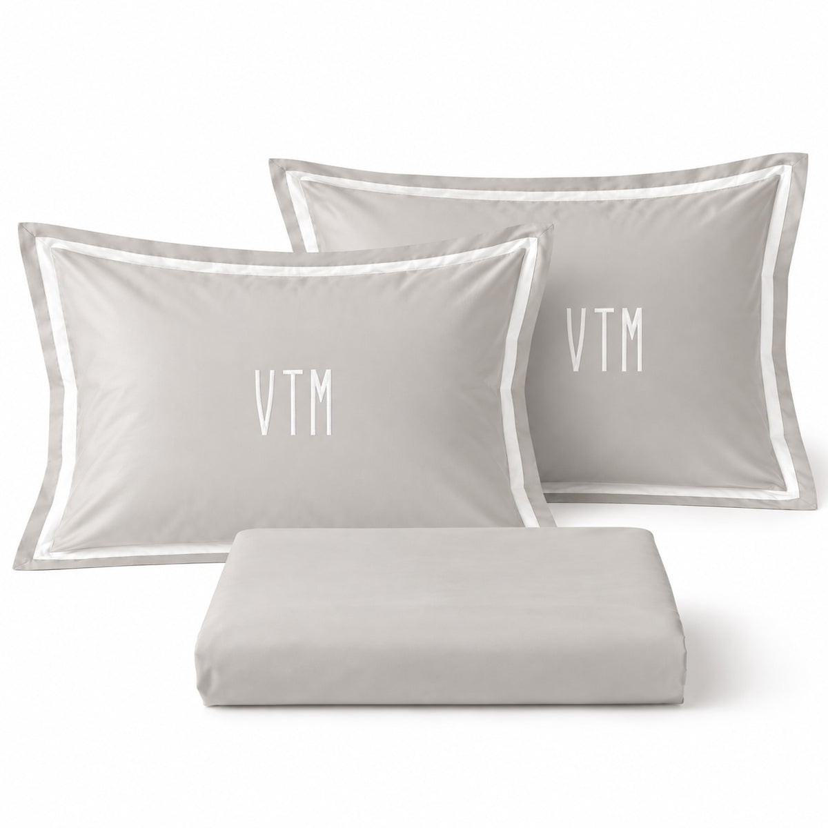 Close-up of TYPEFACE 4 grey sateen pillowcases with white border and white monogram embroidery, with folded sheet