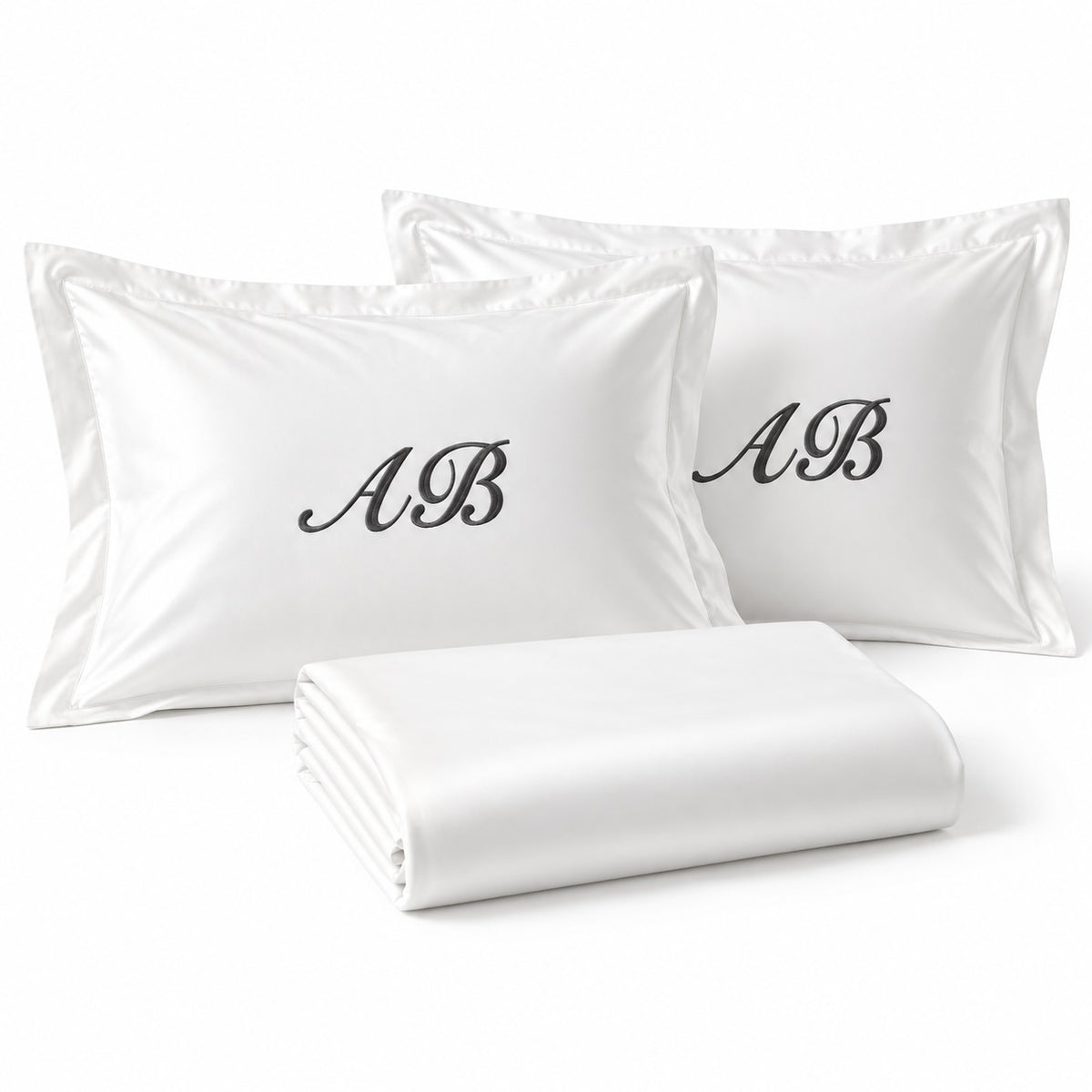 Close-up of TYPEFACE 5 white sateen pillowcases with script monogram embroidery and folded sheet